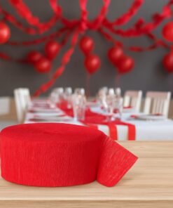 Rødt crepepapir og pakket rød streamer placeret på et rødt bord foran en baggrund med røde streamers, balloner og vimpler i et festligt miljø.
