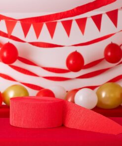 Rødt crepepapir og pakket rød streamer placeret på et rødt bord foran en baggrund med røde streamers, balloner og vimpler i et festligt miljø.