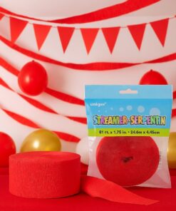 Rødt crepepapir og pakket rød streamer placeret på et rødt bord foran en baggrund med røde streamers, balloner og vimpler i et festligt miljø.