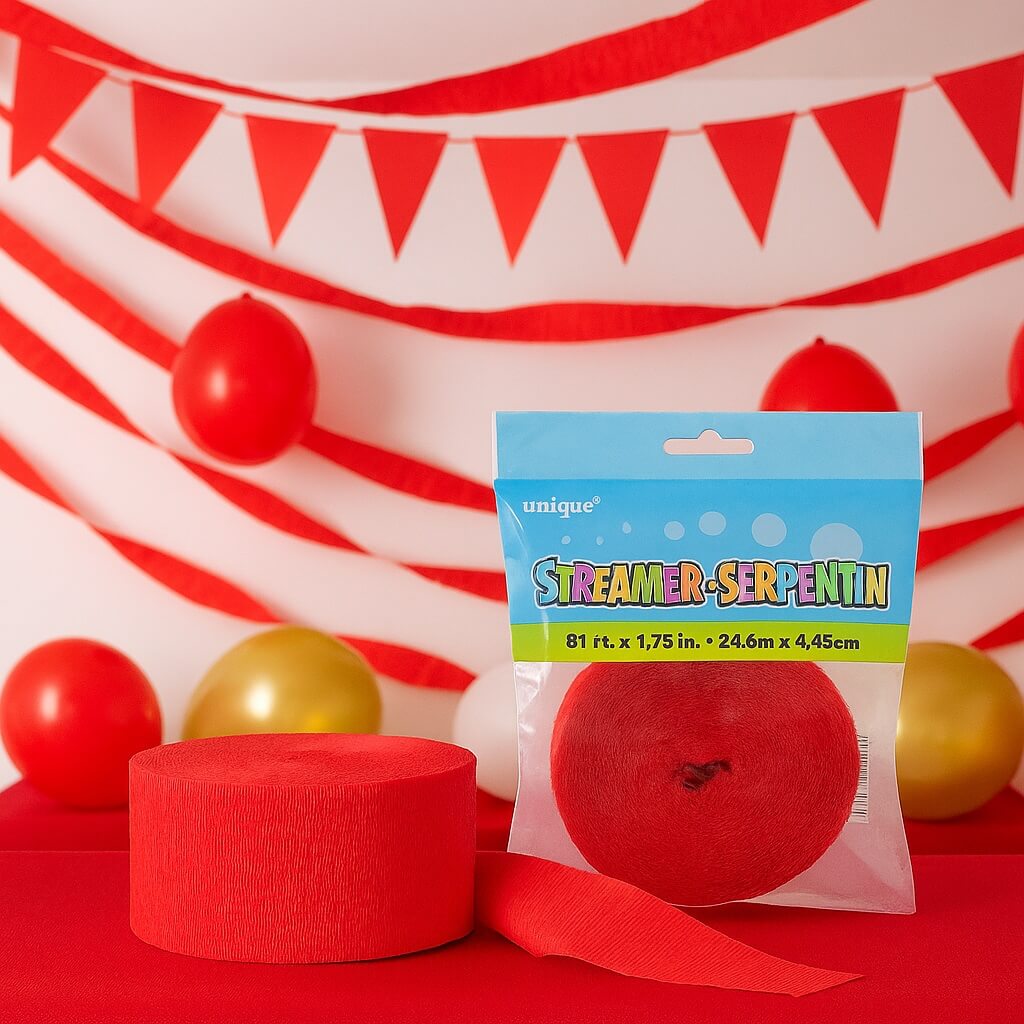 Rødt crepepapir og pakket rød streamer placeret på et rødt bord foran en baggrund med røde streamers, balloner og vimpler i et festligt miljø.
