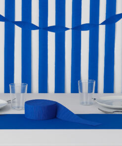 Blåt crepepapir brugt som bordløber og vægdekoration på et festligt dækket bord med tallerkener og glas.