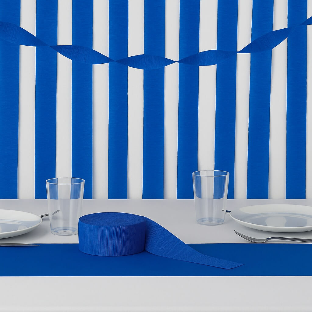 Blåt crepepapir brugt som bordløber og vægdekoration på et festligt dækket bord med tallerkener og glas.