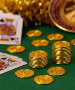 Guld-farvede plastikmønter med dollar-tegn på grønt spillebord med kort og roulette i baggrunden.
