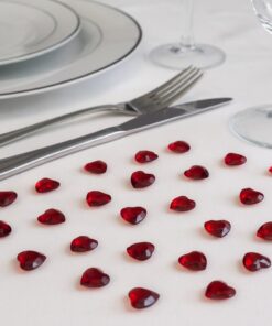 Romantisk bordopdækning med røde roser, bestik og rubinrøde hjerteformede pynte diamanter på hvidt bord.