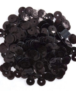 Hvid skål fyldt med sorte palietter, omgivet af spredte palietter på en grå overflade.