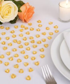 Små guldhjerter spredt på et hvidt festbord med roser, tændt lys og opdækning.