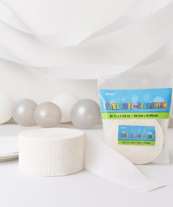 Hvid rulle crepepapir og indpakket streamer-rulle placeret foran balloner og hængende crepepapirsstrimler i et lyst, festligt miljø.