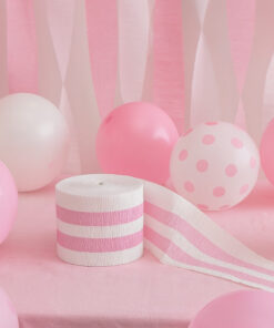 Crepepapir rulle i hvid og lyserød omgivet af lyserøde og hvide balloner på festligt baggrund.