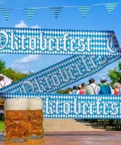 Udendørs Oktoberfest-stemningsbillede med ølkrus, blå/hvidt Oktoberfest-bånd og folk ved festborde i baggrunden.