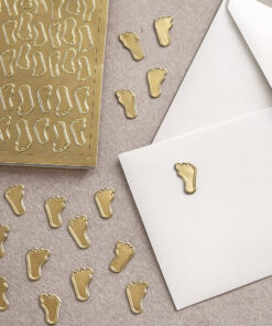 Ark med guldfarvede stickers formet som små babyfødder, velegnet til barnedåb og babyshower dekoration.