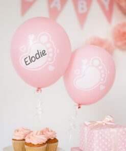 Lyserøde babyshower-balloner med skrivefelt, cupcakes og gaveæske i lyserød pyntet setting.