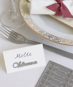 Bordkort med sølv ‘Velkommen’-sticker på elegant opdækning med tallerken, serviet og stickersark.