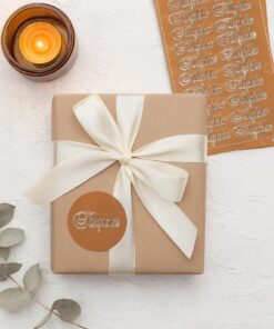 Gave indpakket i kraftpapir med hvid sløjfe og Tillykke sticker i kobber