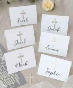 Bordkort med sølvkors-stickers og håndskrevne navne, omgivet af blomst, eukalyptus og dekorativt bånd.