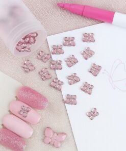Lyserøde facetslebne sommerfugl-rhinsten brugt til nail art og DIY, vist sammen med negletips, pink tusch og papir.