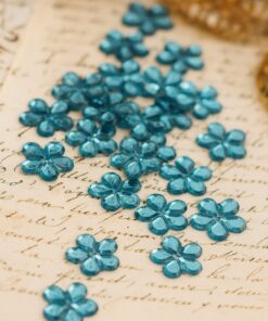 Lyseblå blomsterformede facetslebne rhinsten på gammelt håndskrevet papir.