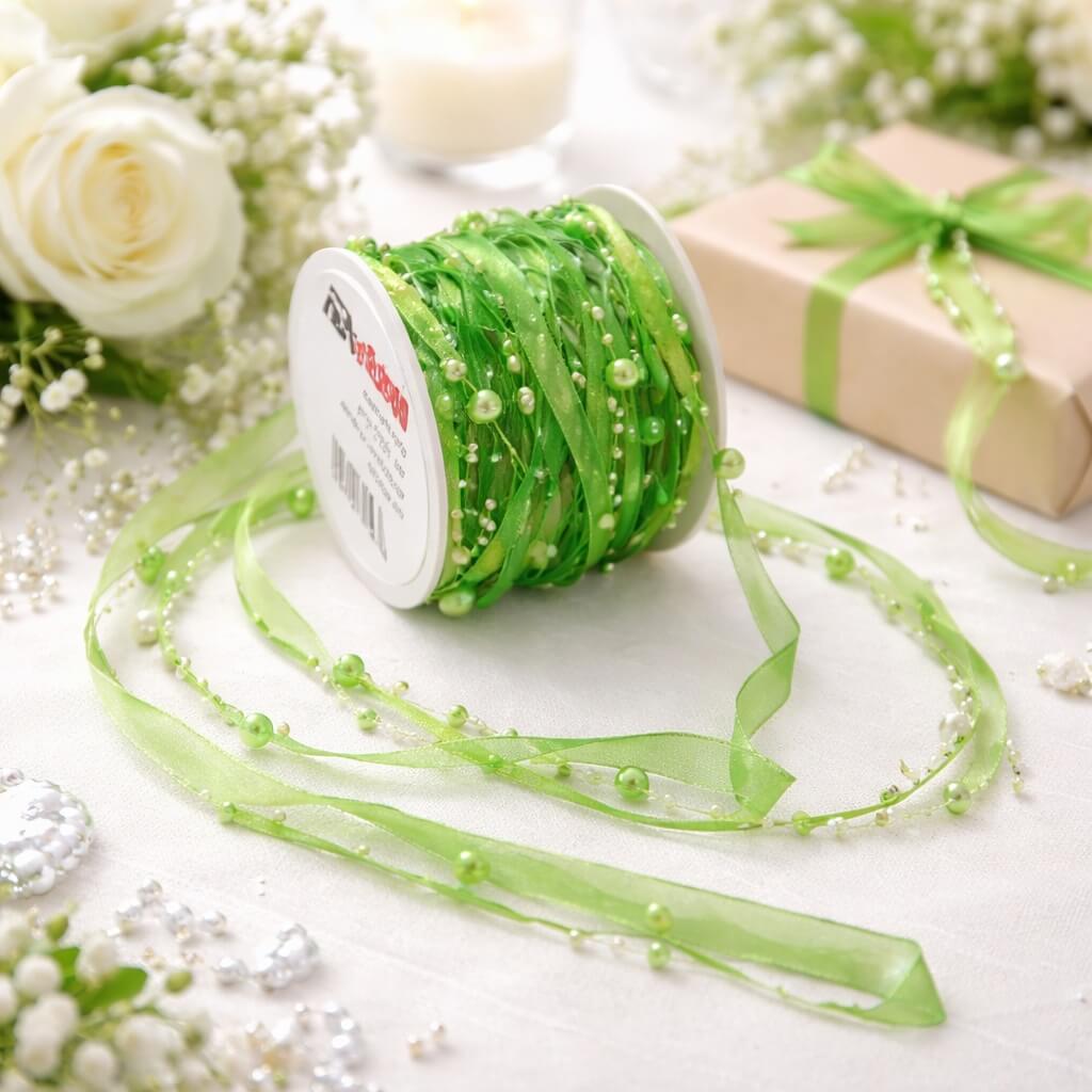 Grønt satinbånd med perler på rulle, delvist udrullet på festbord med blomster og gavepynt