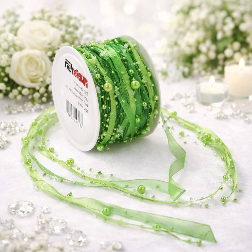 Grønt satinbånd med perler på rulle, delvist udrullet på lyst underlag med dekorativ baggrund
