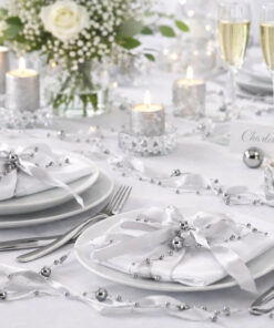 Elegant borddækning med sølvfarvet satinbånd med perler, hvide tallerkener og stearinlys