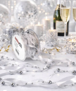 Sølvfarvet satinbånd med perler rullet ud på festbord med lys, konfetti og champagneglas