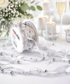 Sølvfarvet satinbånd med perler rullet ud på festbord med stearinlys og champagneglas