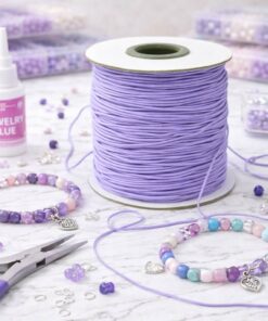 Smykkefremstilling med lilla elastiksnor, perlearmbånd, perler og værktøj på kreativ arbejdsflade.