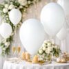 Hvide balloner til festpynt ved dækket festbord med blomster og champagneglas
