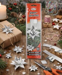 Person folder flettede julestjerner af sølv stjernestrimler ved julebord med gran, lys, gave og hobbyredskaber