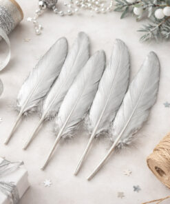 Seks sølvfarvede dekorationsfjer brugt i kreativ DIY dekoration med gave, snor og pynt på lyst underlag