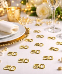 Close-up af festbord til 50 år med guld tal konfetti “50”, borddækning i hvid og guld samt champagneglas