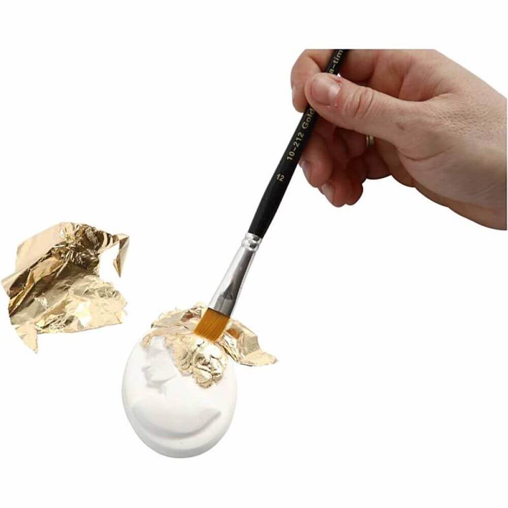 Bladmetal guld, tynde dekorationsark i metallisk guld, der påføres en hvid genstand med en pensel i et kreativt DIY-projekt.