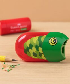 Faber-Castell dobbelt blyantspidser med rød og grøn fiskedekoration placeret på et bord med blyant og spåner.
