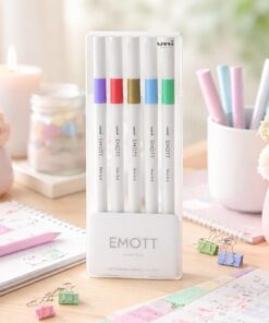 Uni Ball EMOTT fineliners på lyst pastel skrivebord med bullet journal og kreative kontorartikler.